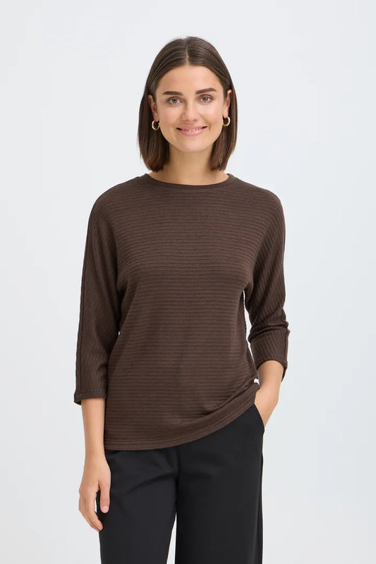 A woman modeling a dark brown ribbed knit long-sleeve top with black pants, standing against a light gray studio background.