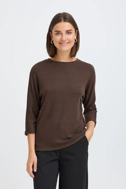 A woman modeling a dark brown ribbed knit long-sleeve top with black pants, standing against a light gray studio background.