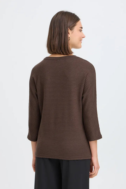 dark brown long-sleeve ribbed knit top with black wide-leg trousers and dark brown flats, standing against a light gray studio background.