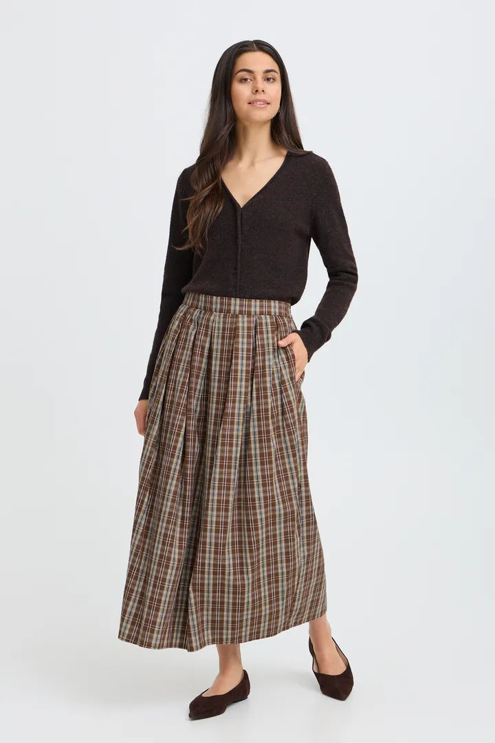 A woman modeling a dark brown long-sleeve knit cardigan and a brown, beige, and gray plaid midi skirt with pockets, paired with dark brown flats, against a light gray studio background.