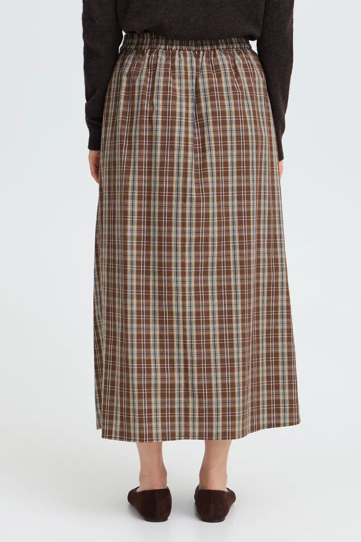 A person shown from the back wearing a brown, beige, and white plaid midi skirt with an elastic waistband, paired with a dark brown sweater and dark brown flat shoes, against a light gray studio background.