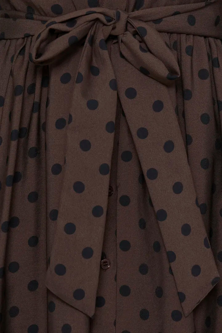 Close-up of a brown fabric garment with dark navy polka dots and a matching tie belt.