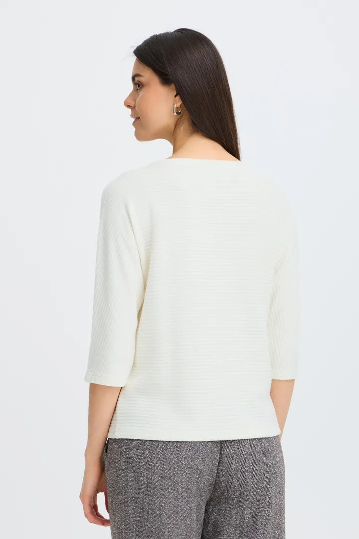 A woman shown from the back wearing a cream ribbed knit three-quarter sleeve top and gray textured trousers, photographed against a clean white studio background.