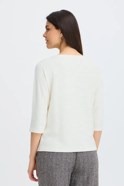 A woman shown from the back wearing a cream ribbed knit three-quarter sleeve top and gray textured trousers, photographed against a clean white studio background.
