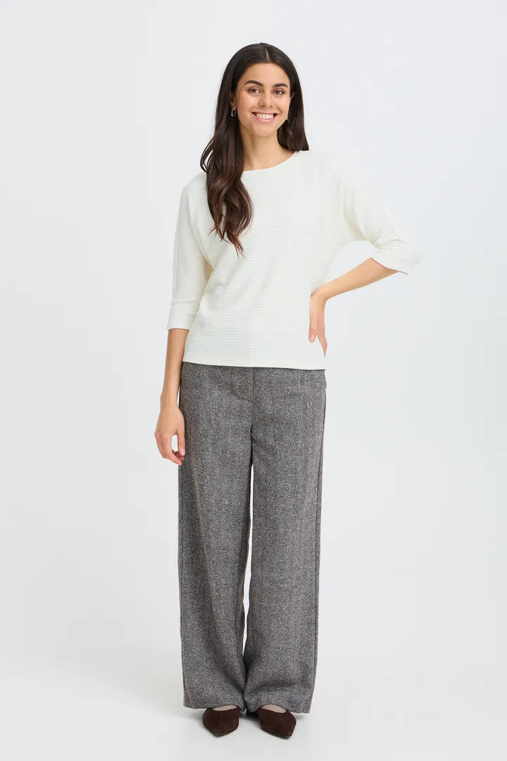 A woman modeling a cream-colored three-quarter sleeve top and gray wide-leg trousers against a plain white studio background.