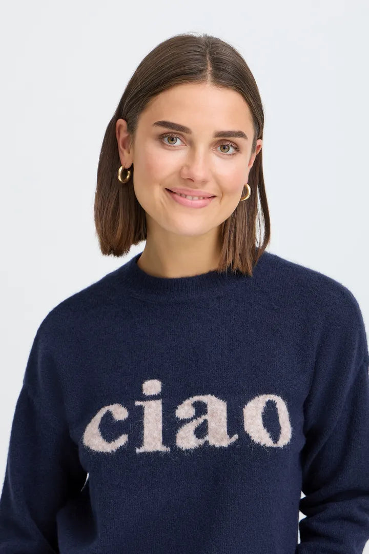 A woman with shoulder-length brown hair wearing a navy blue knit sweater with the word 'ciao' in a fuzzy cream-colored lettering across the chest, set against a plain light gray background.