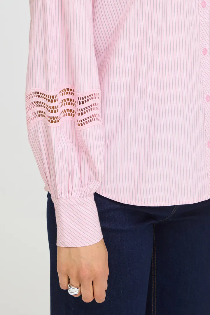 A close-up of a pink and white striped long-sleeve blouse with eyelet lace detailing on the upper sleeve, worn with dark blue jeans.