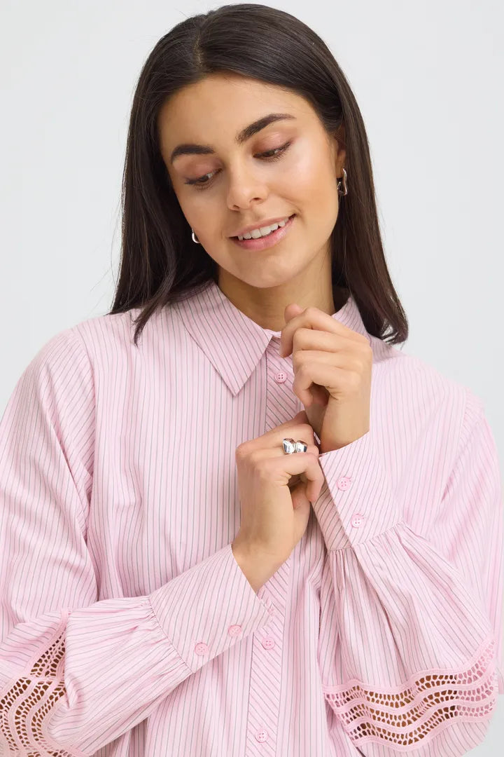 Woman wearing a pink striped shirt with lace details on a light gray background