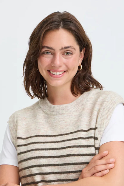 A smiling woman with shoulder-length brown hair wearing a sleeveless knit sweater vest with horizontal dark brown stripes over a white t-shirt, set against a plain light gray background.
