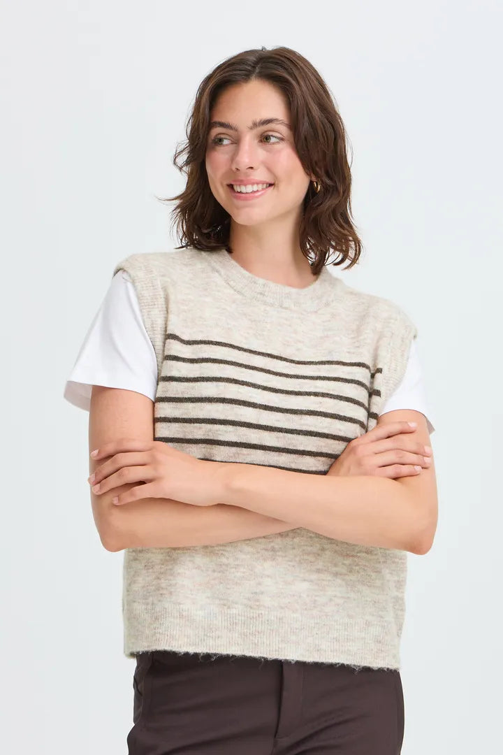 A woman modeling a sleeveless knit sweater vest with horizontal stripes in beige and brown over a white t-shirt, set against a plain light gray background.