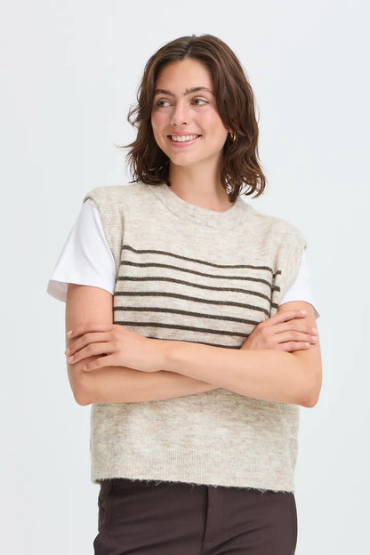 A woman modeling a sleeveless knit sweater vest with horizontal stripes in beige and brown over a white t-shirt, set against a plain light gray background.
