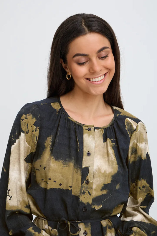 A woman wearing a long-sleeve button-front top with a black and beige abstract watercolor-style print, shown against a plain light gray studio background.