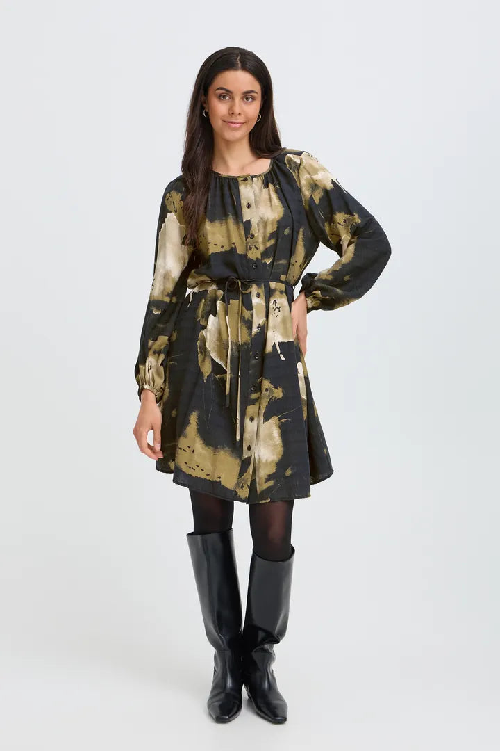 A woman modeling a long-sleeve mini dress with a black and beige abstract tie-dye pattern, paired with black tights and black knee-high boots, against a light gray studio background.
