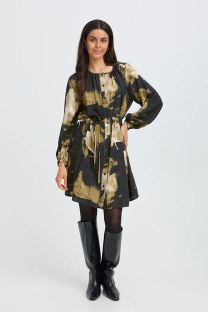 A woman modeling a long-sleeve mini dress with a black and beige abstract tie-dye pattern, paired with black tights and black knee-high boots, against a light gray studio background.