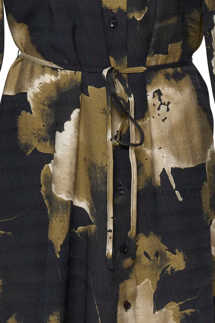 Close-up of a button-front garment with a tie waist and an abstract painterly print in black, beige, and olive-brown tones.