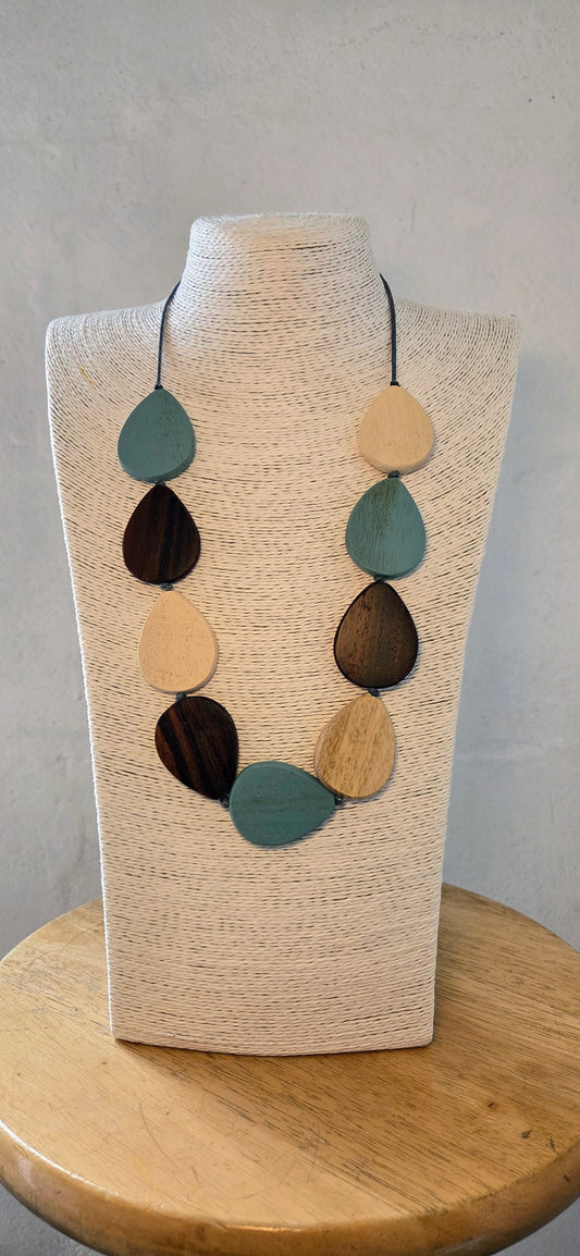 Necklace with blue  multicolored leaf-shaped pendants on a wooden stand against a grey background
